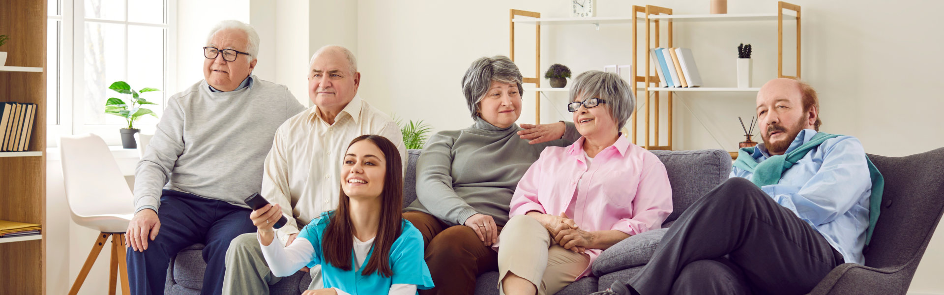 Group of elderly and one caretaker sitting down watching television
