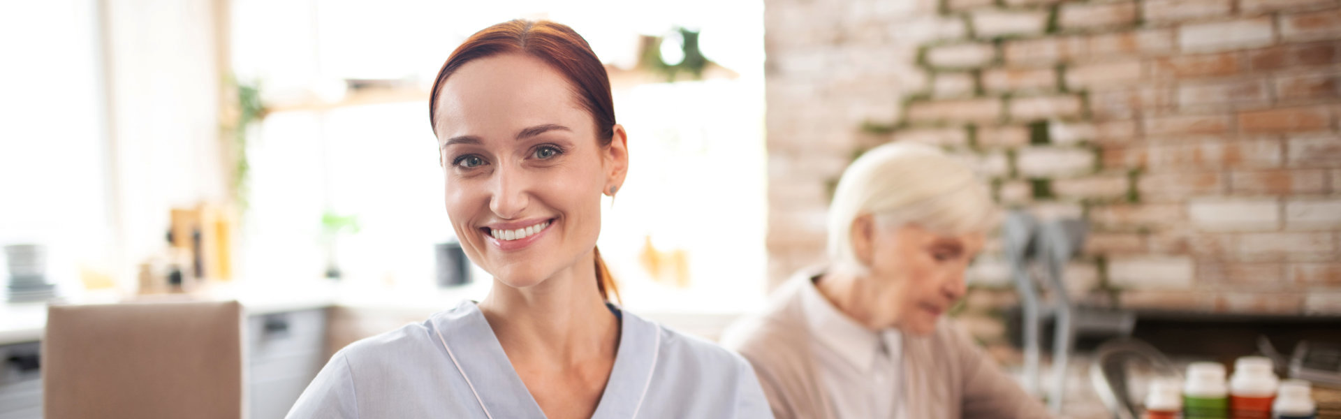 caregiver smiling with an elderly woman behind her